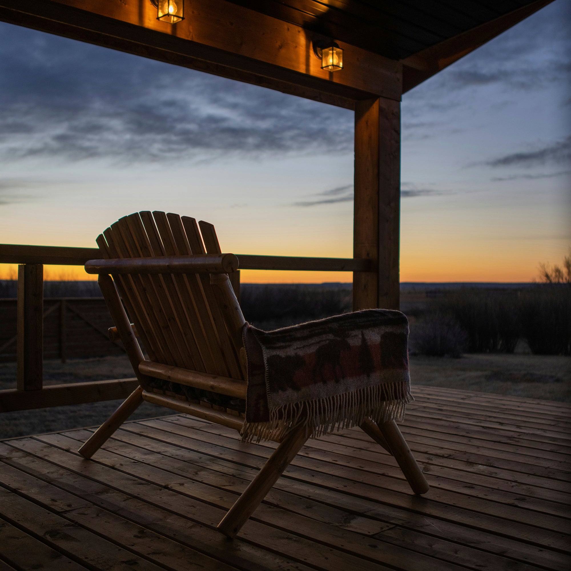 Western-style porch at sunset with accent chair, rustic lanterns, and golden light