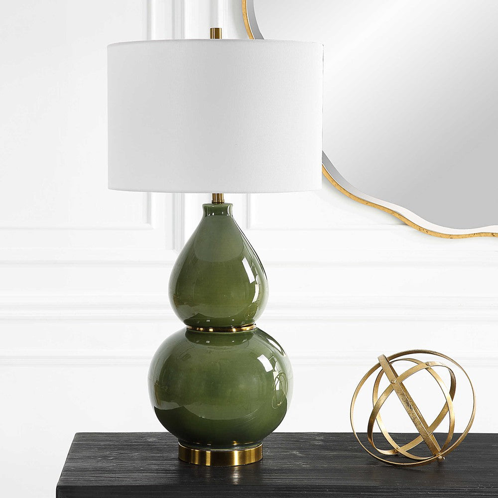 This Gourd Table Lamp is an elegant piece worthy of any home. Crafted with a timeless gourd shaped ceramic base, it features a moss green glaze accented with lightly antiqued brass plated details. The round drum shade is made from white linen fabric, giving the lamp a soft and inviting feel. Due to the unique nature of fired glazes on ceramic lamps, each lamp has an individual finish.