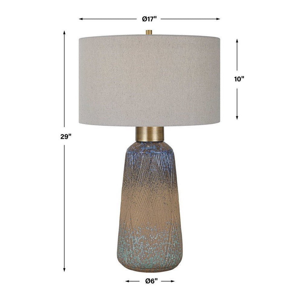 A beautiful display of color and style, this ceramic table lamp features an embossed design with a unique mix of matte and gloss glazes in various shades of blue-green, indigo, and golden rust, paired with antique brass plated details. The hardback drum shade is covered in a light gray linen fabric with natural slubbing.