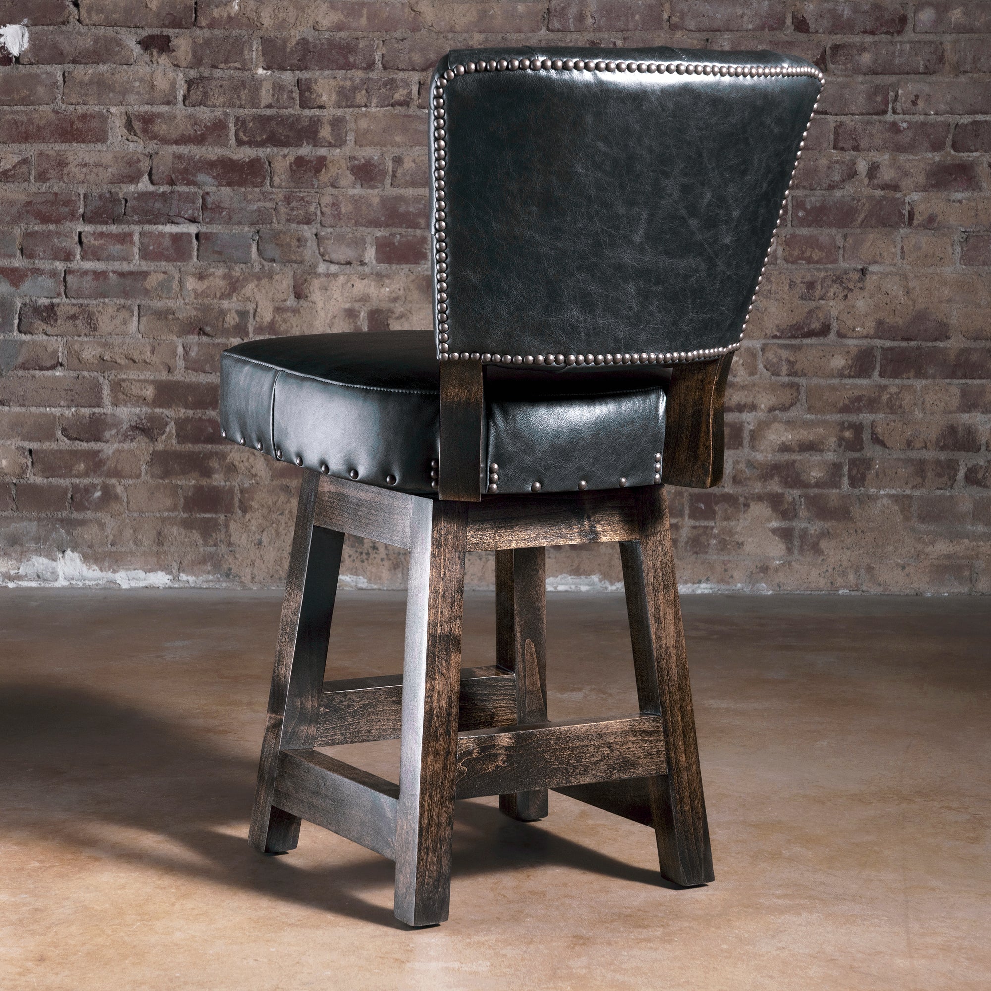 Back view of black leather bar stool with nailhead-trimmed back and dark stained alder wood legs—upscale Western bar stool