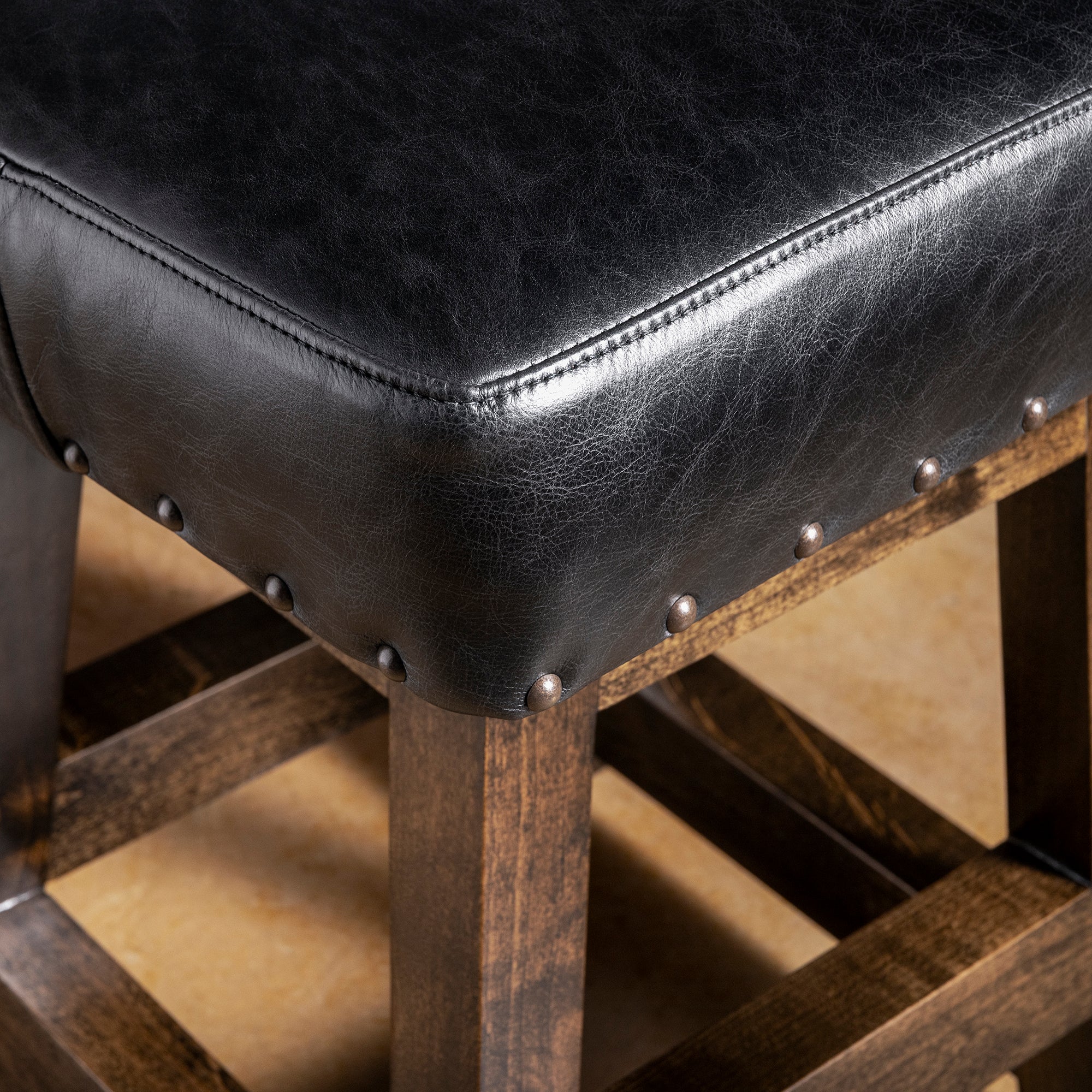 Close-up of black leather bar stool seat with nailhead trim and dark stained alder wood frame—Western counter or bar seating