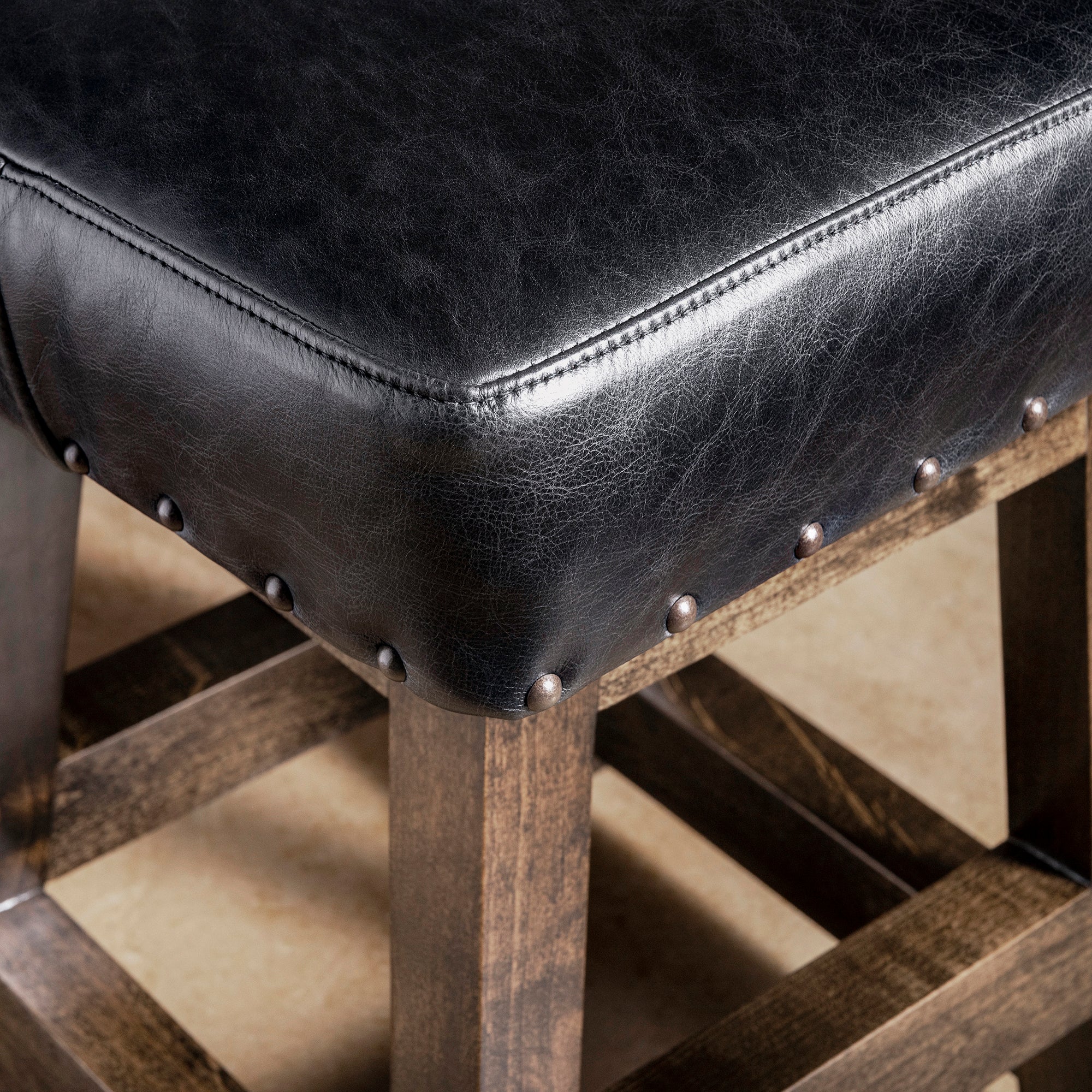 Close-up of black leather bar stool seat with nailhead trim and dark stained alder wood frame—Western counter or bar seating