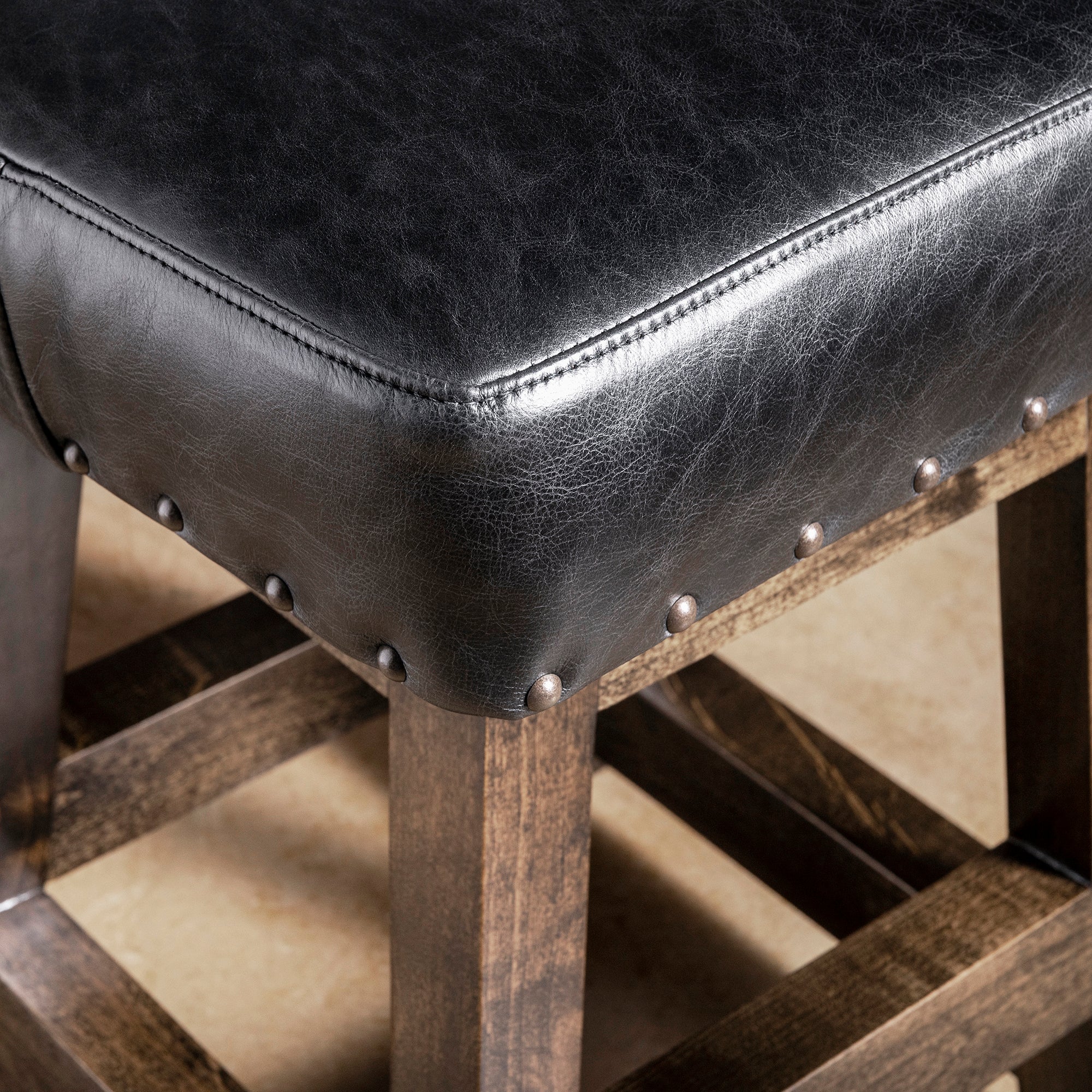 Close-up of black leather bar stool seat with nailhead trim and dark stained alder wood frame—Western counter or bar seating