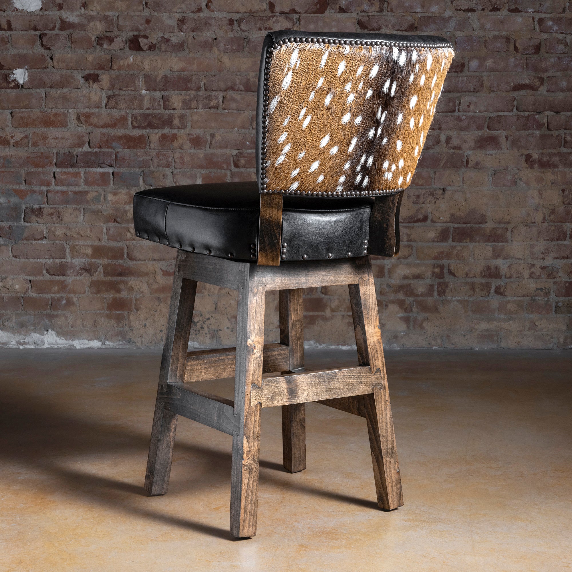 Back view of bar stool with hair-on axis hide panel and nailhead trim, black leather seat and Alder wood base