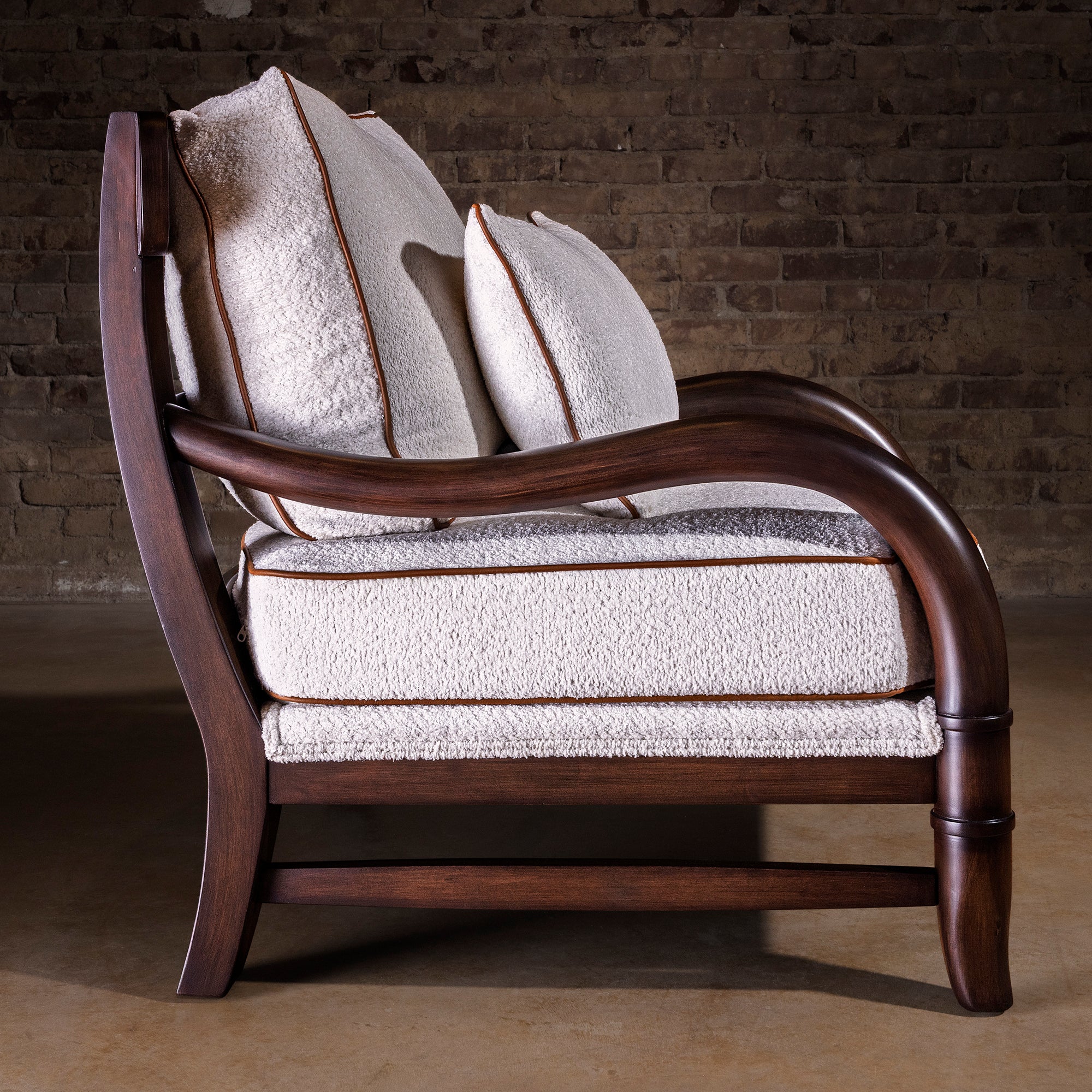 Profile view of bouclé lounge chair with curved wood arms and deep cushions