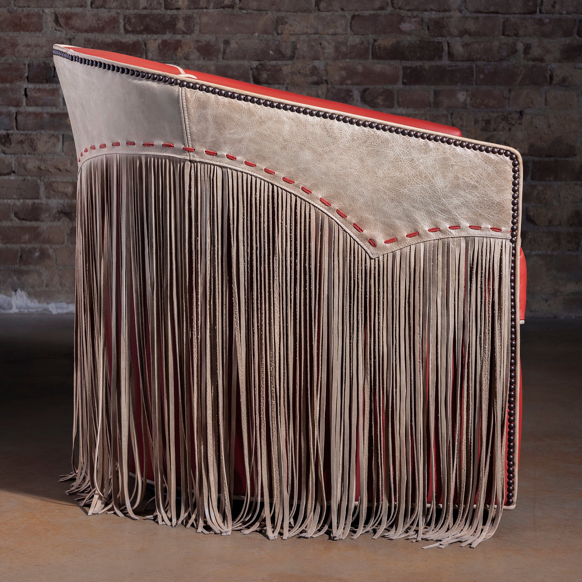 Profile view of coral-red leather barrel swivel chair with fringe and nailhead trim
