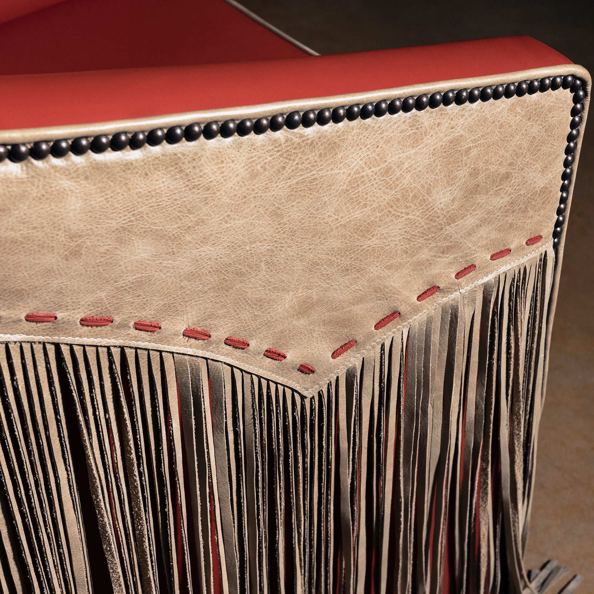 Closeup of taupe leather outside arm with coral red lacing and nailhead trim