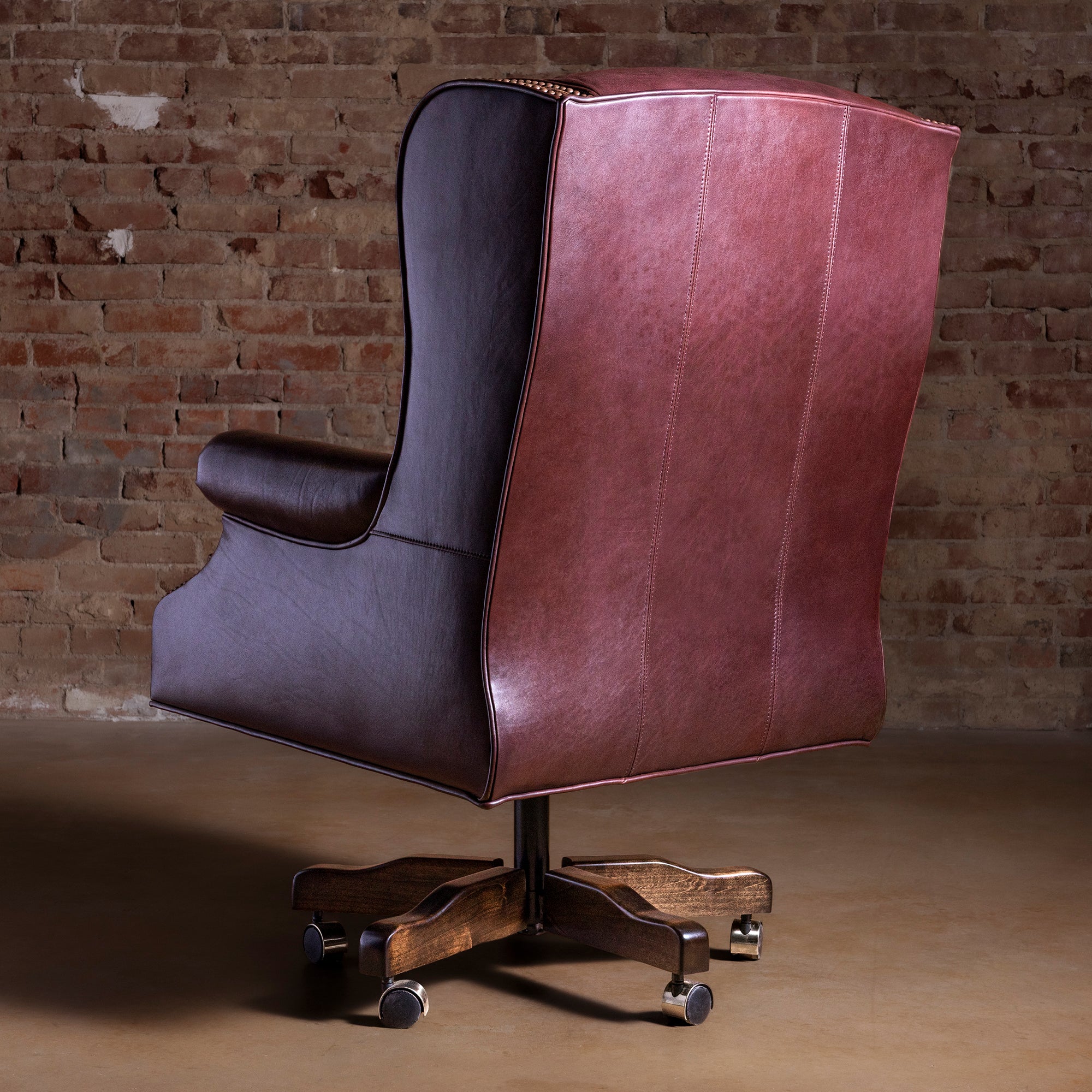 Wingback leather desk chair back view showing high back, tailored arms, and wood base with casters