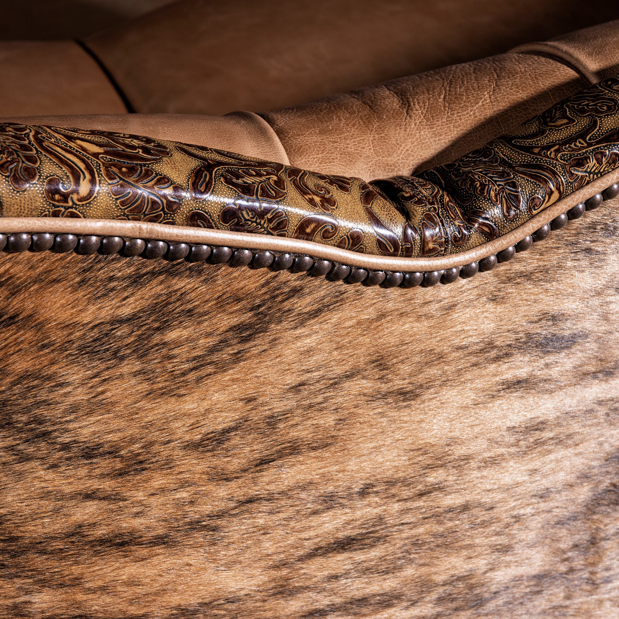 Nailhead detail framing tooled leather and cowhide accents on luxury Western sofa