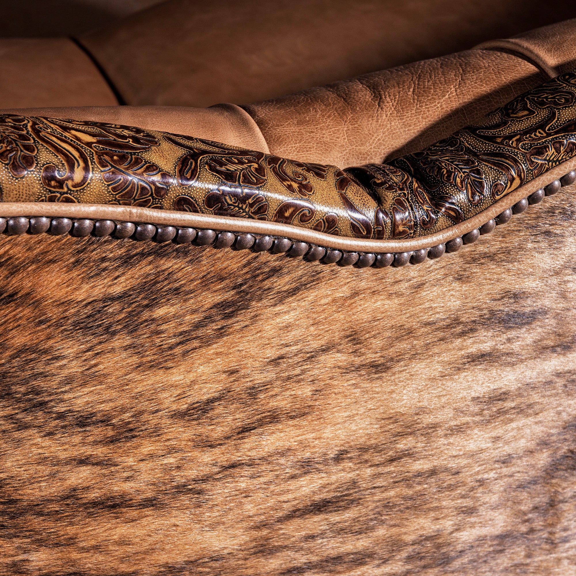 Nailhead detail framing tooled leather and cowhide accents on luxury Western sofa