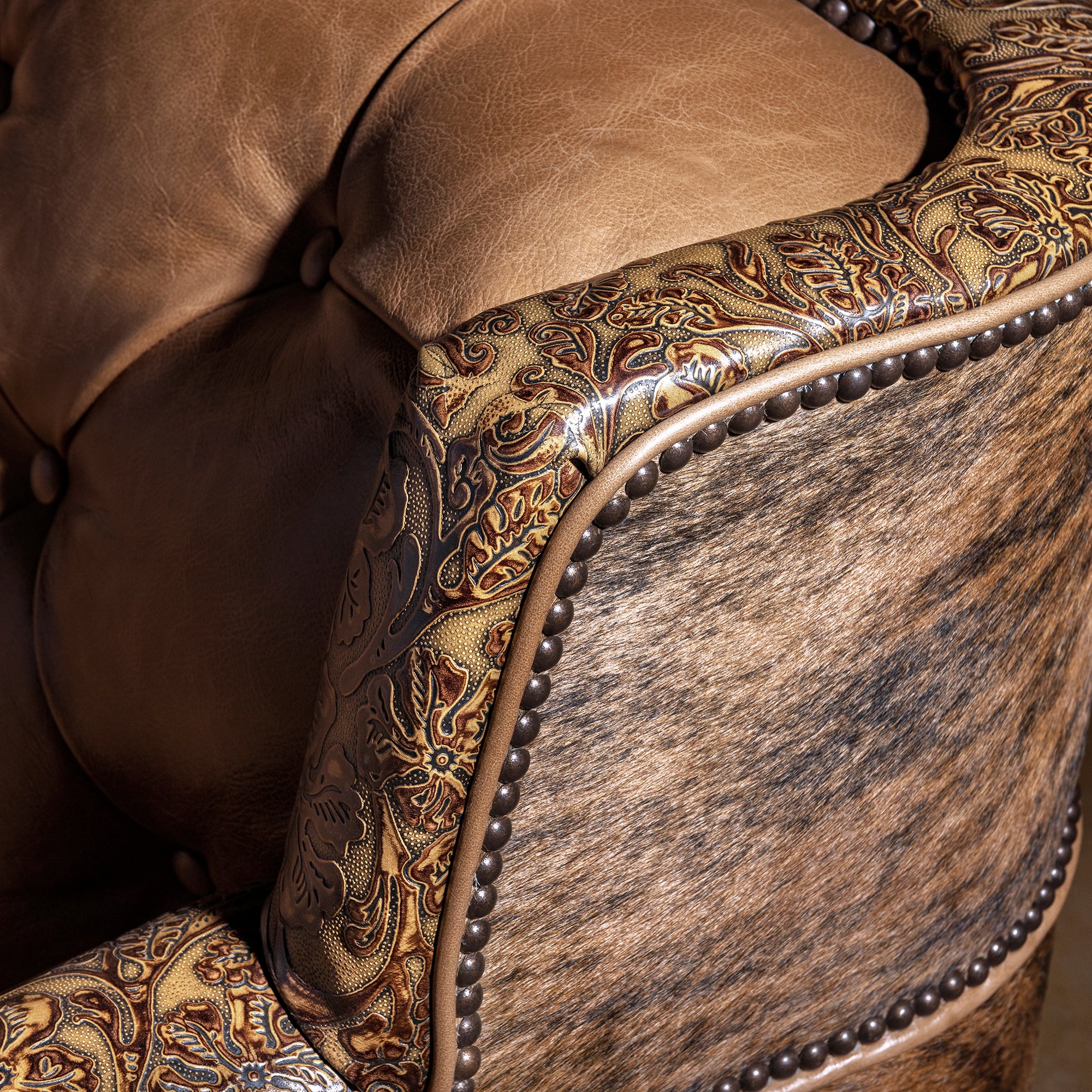 Tooled leather top rail detail on scalloped-back Western tufted leather sofa