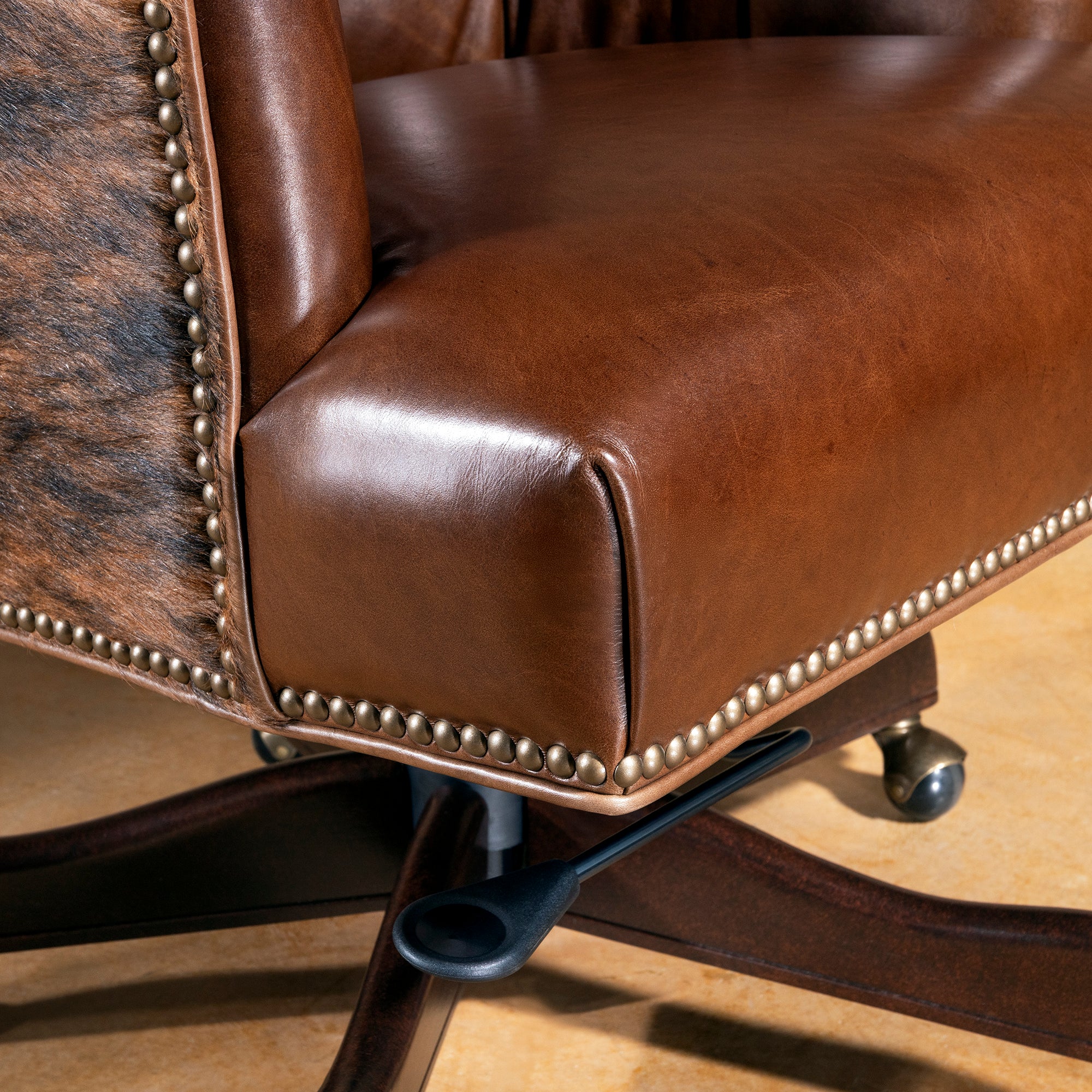 Close-up of brown leather seat, nailhead trim, and brindle cowhide side panel on swivel desk chair