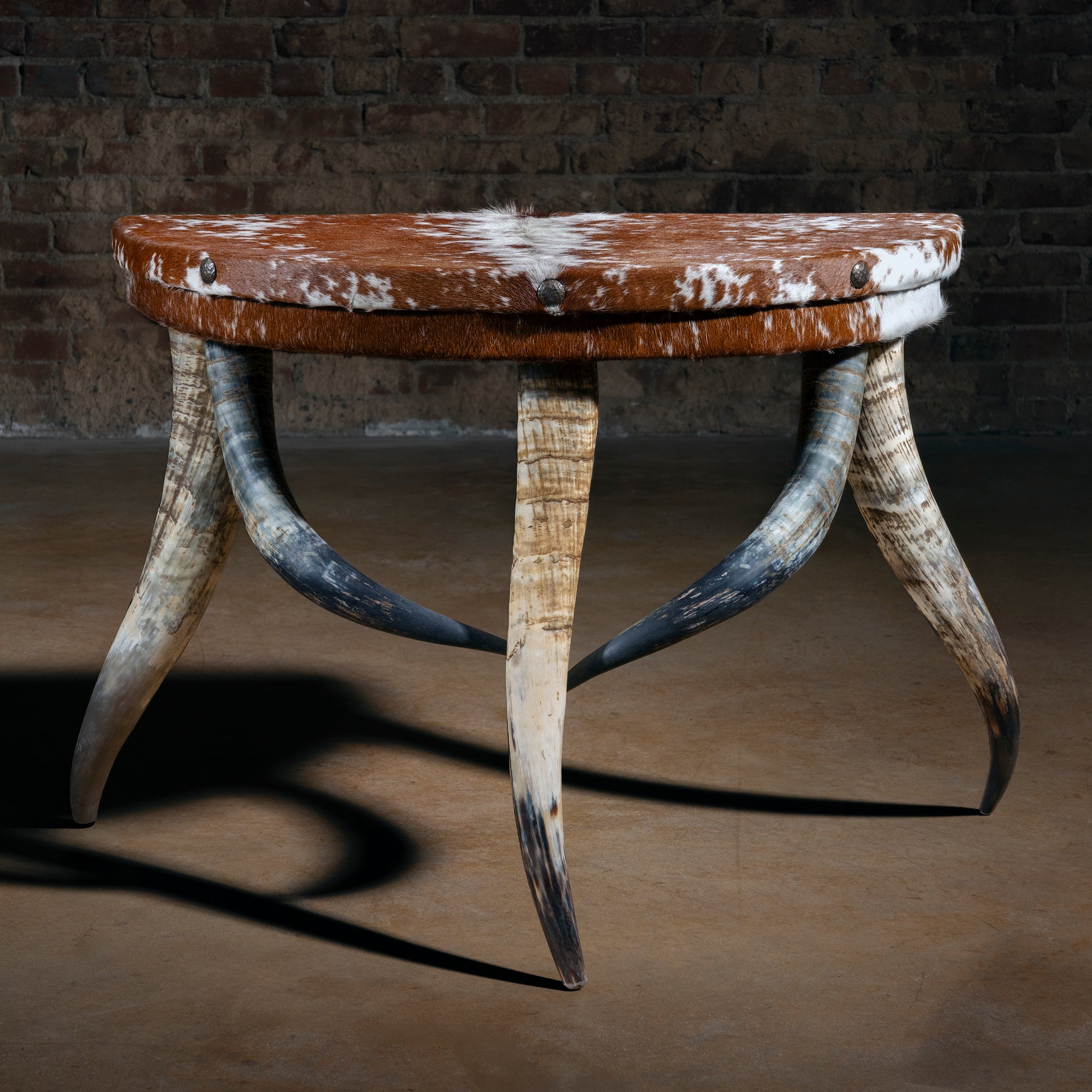 Half-moon cowhide accent table with sculptural bullhorn legs and nailhead trim