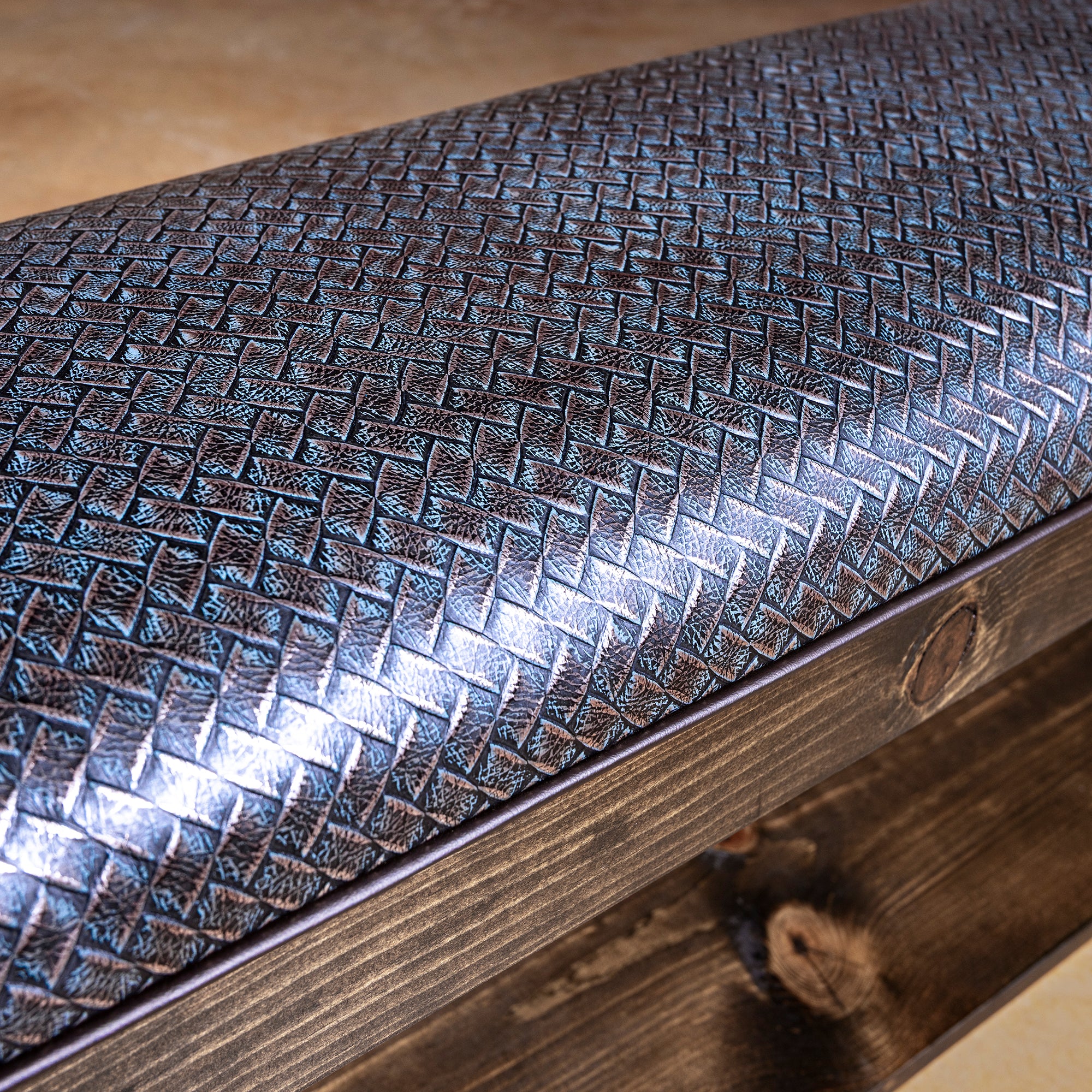Closeup of silver-blue basketweave embossed leather cushion on Western wood bench with piping detail
