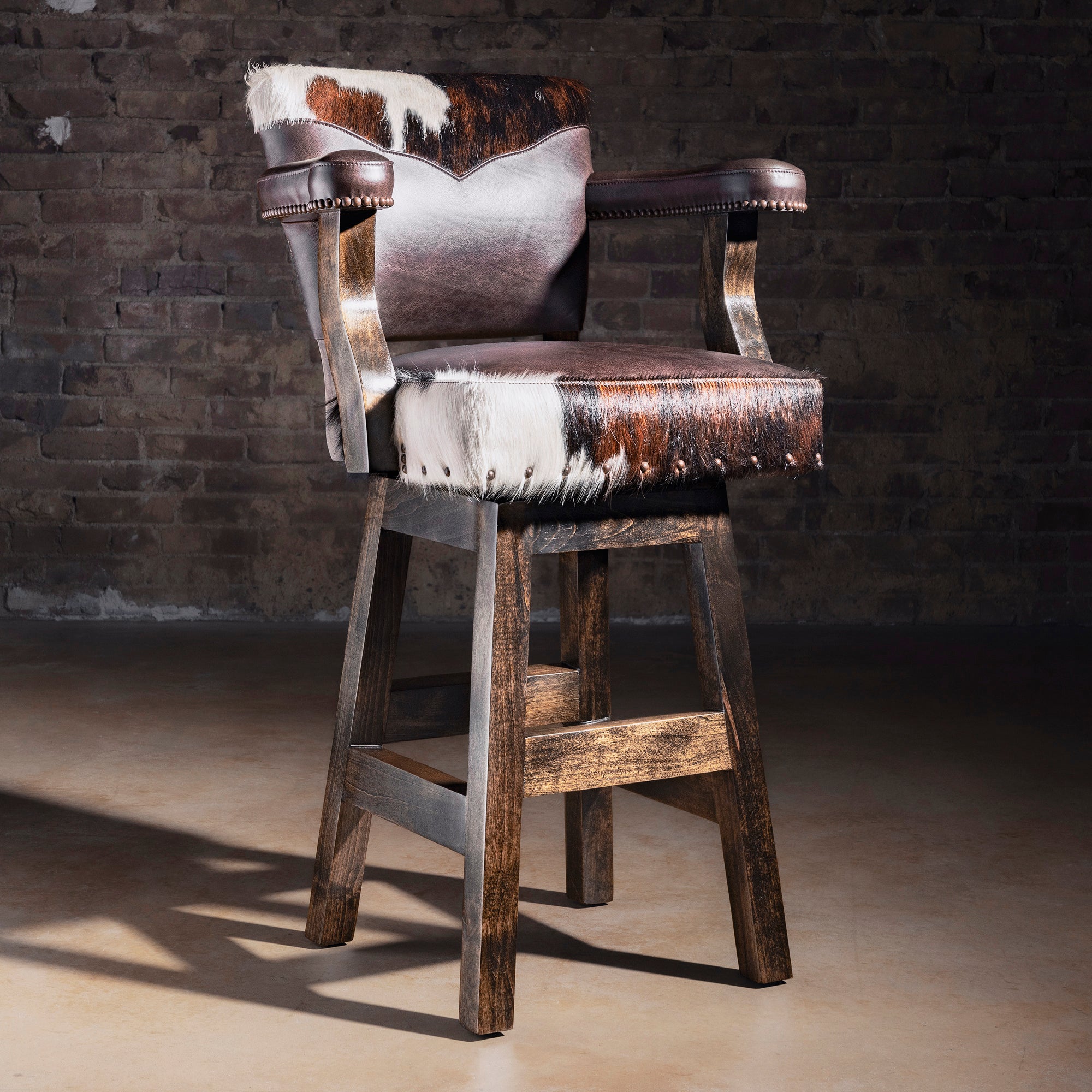 Cochise tricolor Brazilian cowhide and dark leather Western bar stool with arms, nailhead trim, and rustic Alder wood base