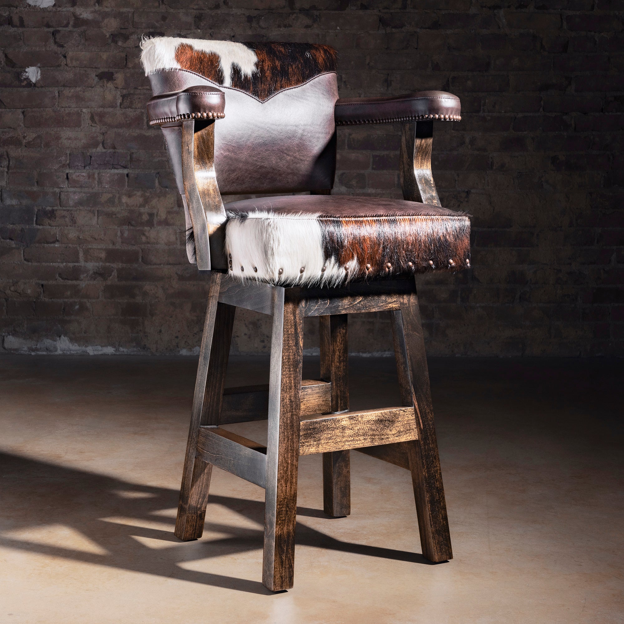 Cochise tricolor Brazilian cowhide and dark leather Western bar stool with arms, nailhead trim, and rustic Alder wood base