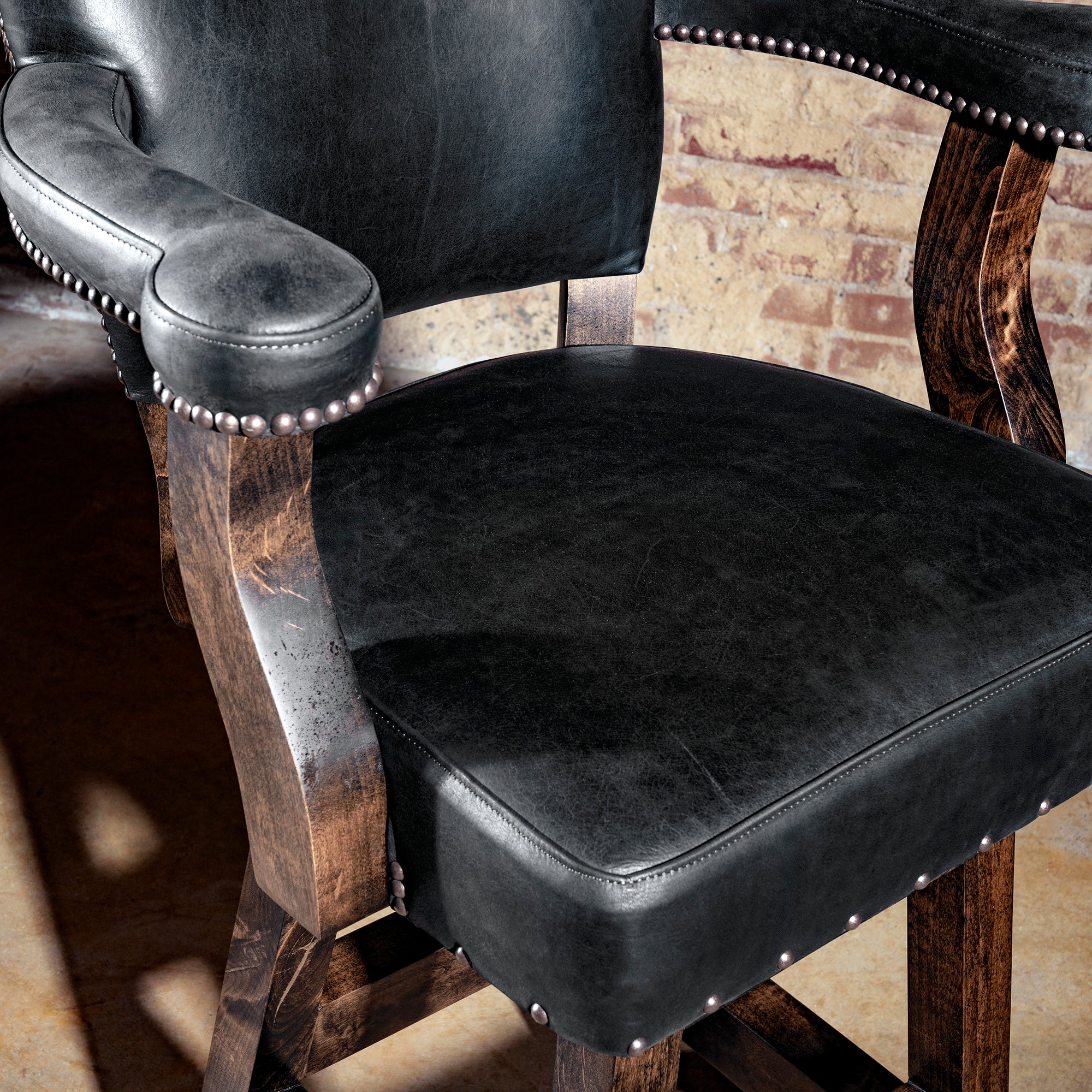 Close-up of black leather seat and armrest with hand-applied nailhead trim on wood frame.