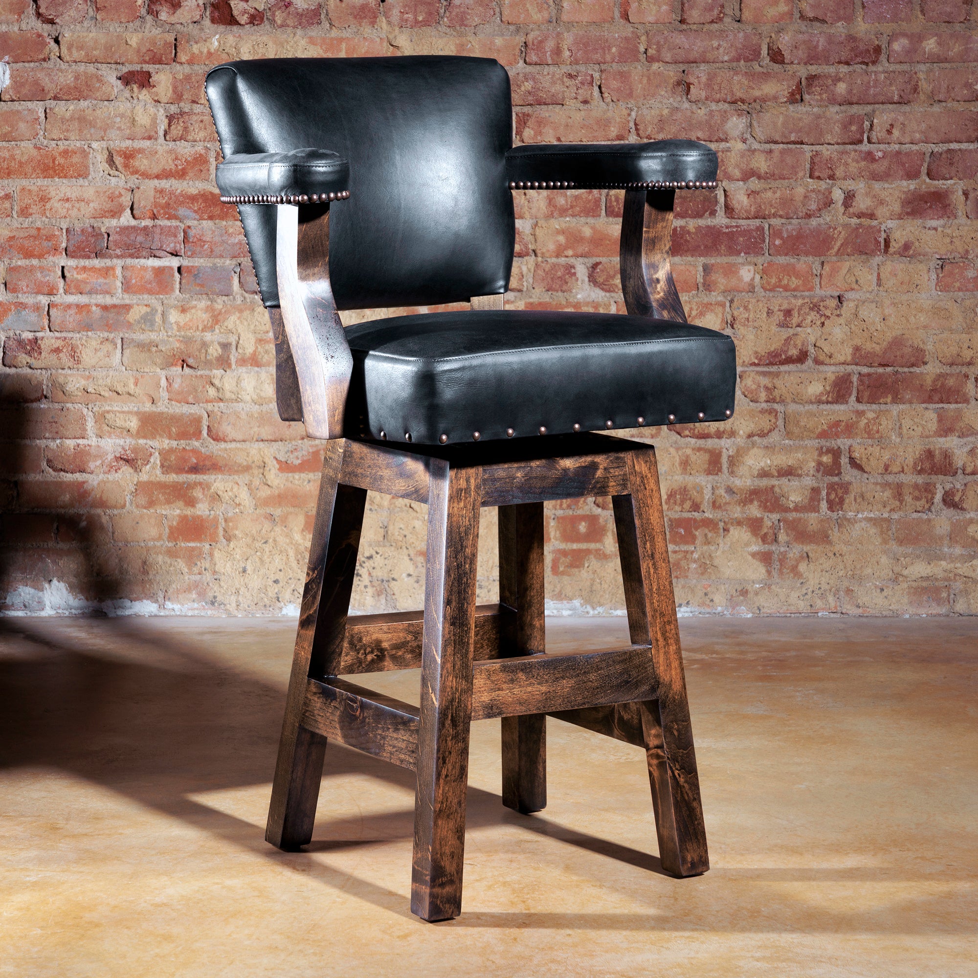 Western swivel bar stool in black leather and axis hide with wooden base, styled against brick wall.