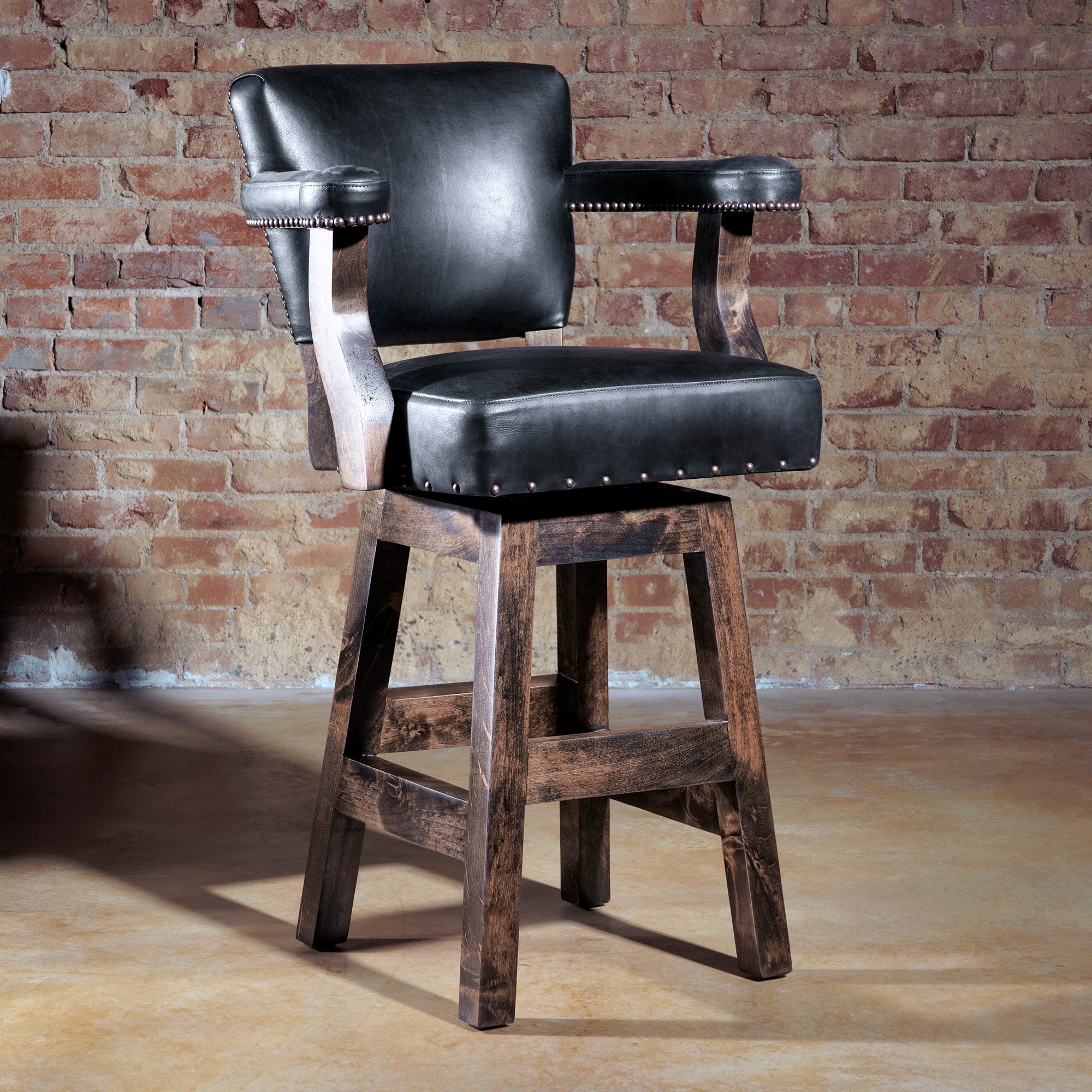 Western swivel bar stool in black leather and axis hide with wooden base, styled against brick wall.