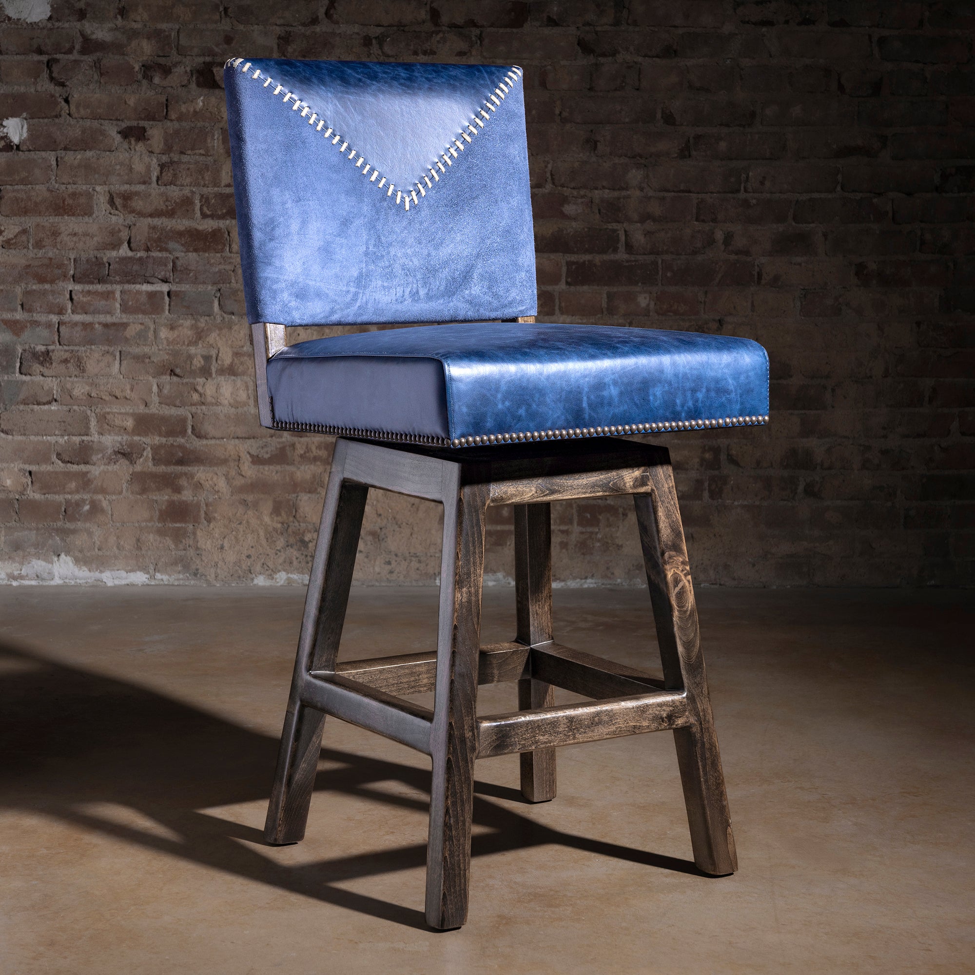 Armless Western bar stool in indigo leather with yoke-stitched back, nailhead trim, and dark wood base
