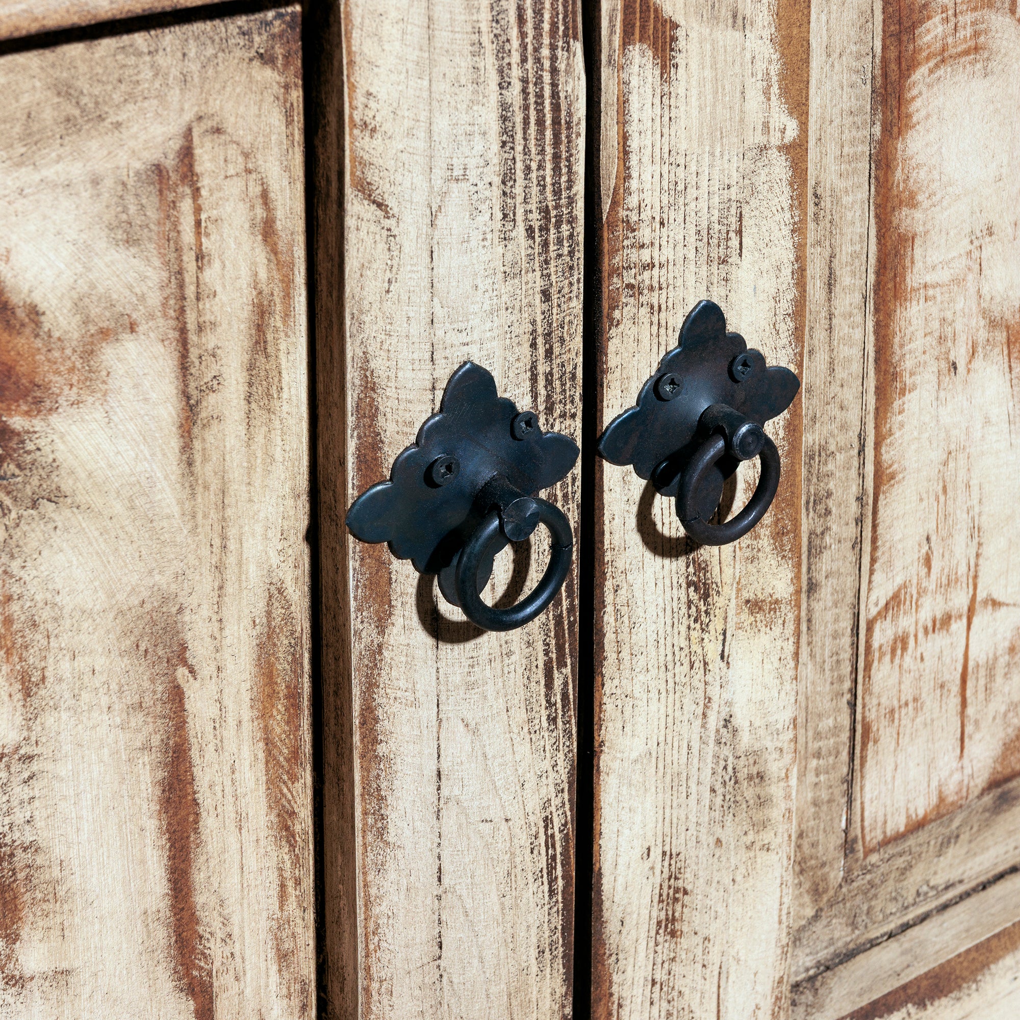 Close-up of black iron ring handles on distressed whitewashed doors