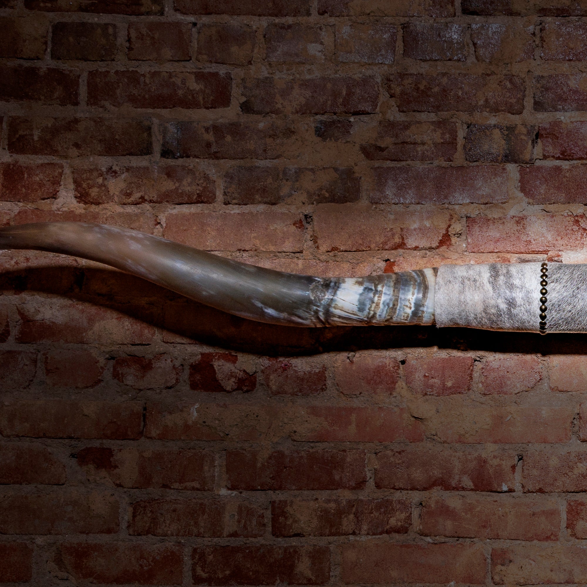 Close-up of horn mount showing patina finish and leather wrap with brass nailheads
