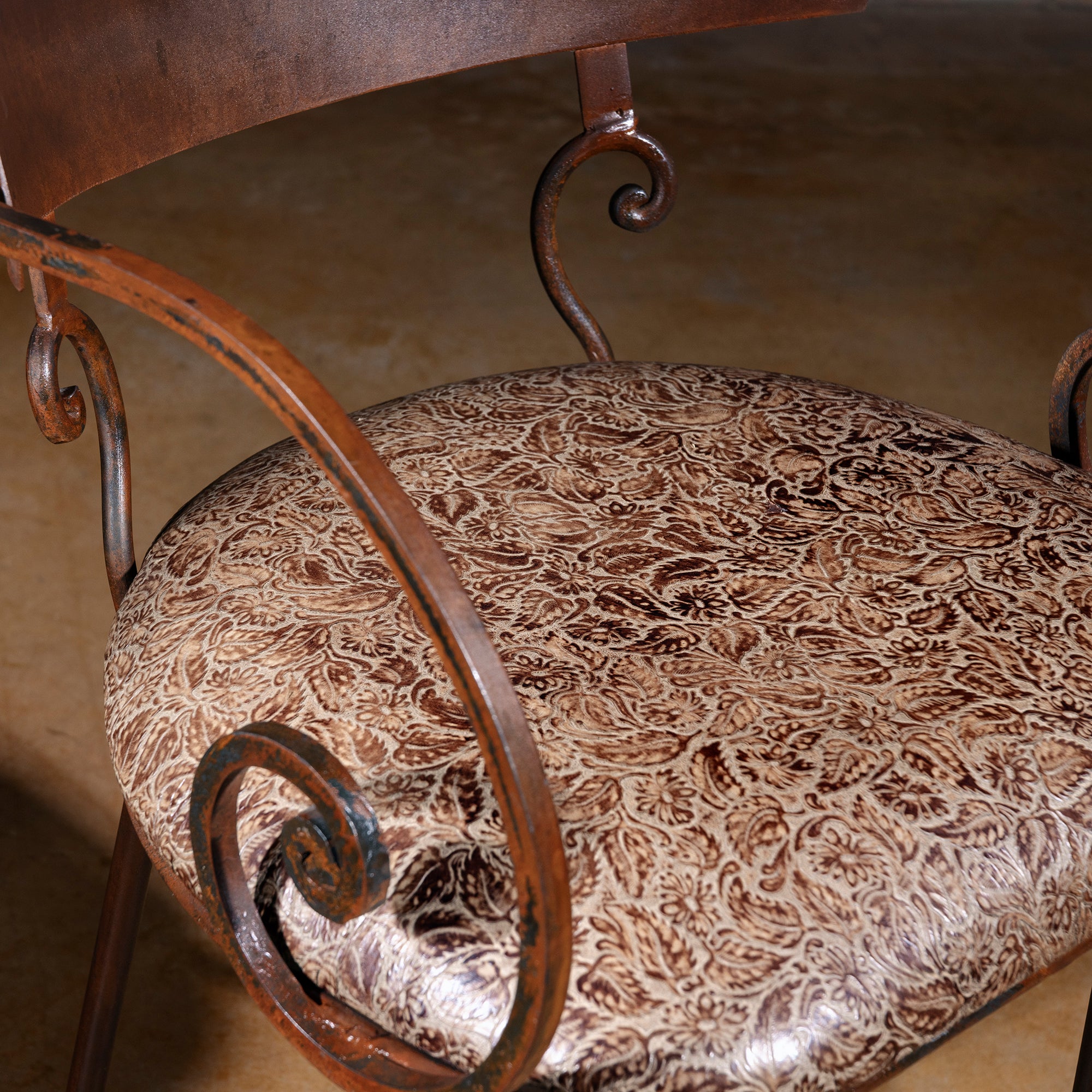Close-up of tooled leather patterned seat and forged iron scroll arm detail on Western bar stool