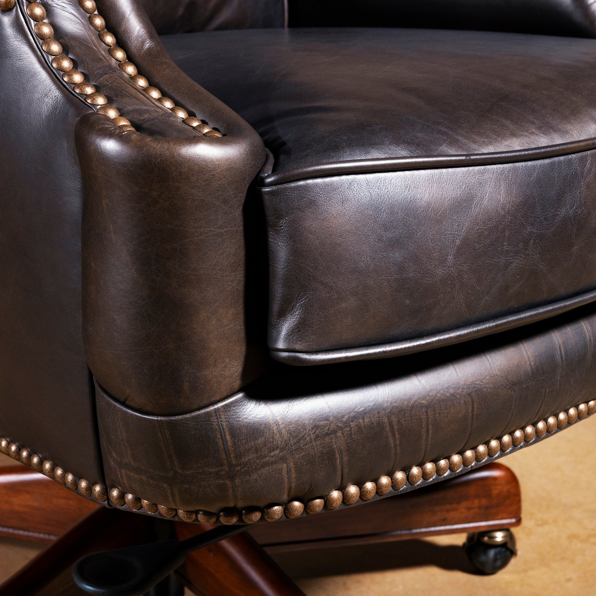 Close-up of leather seat cushion and nailhead base trim on swivel executive desk chair with rolling casters.