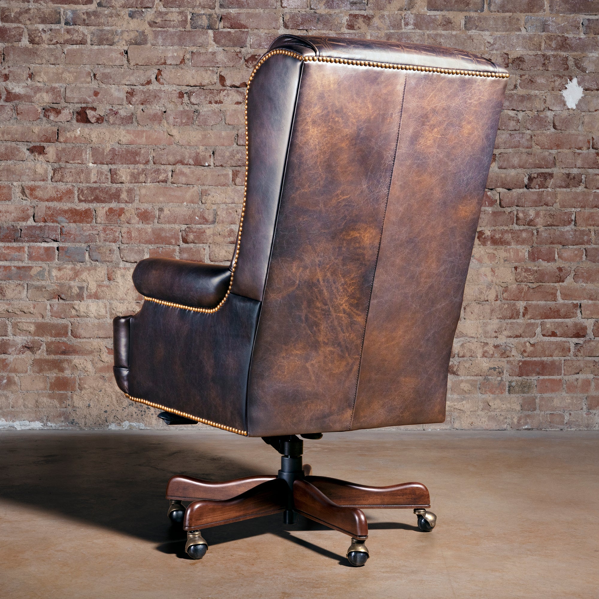 Back view of Western leather desk chair showing tall executive back, nailhead trim, and wood rolling base.