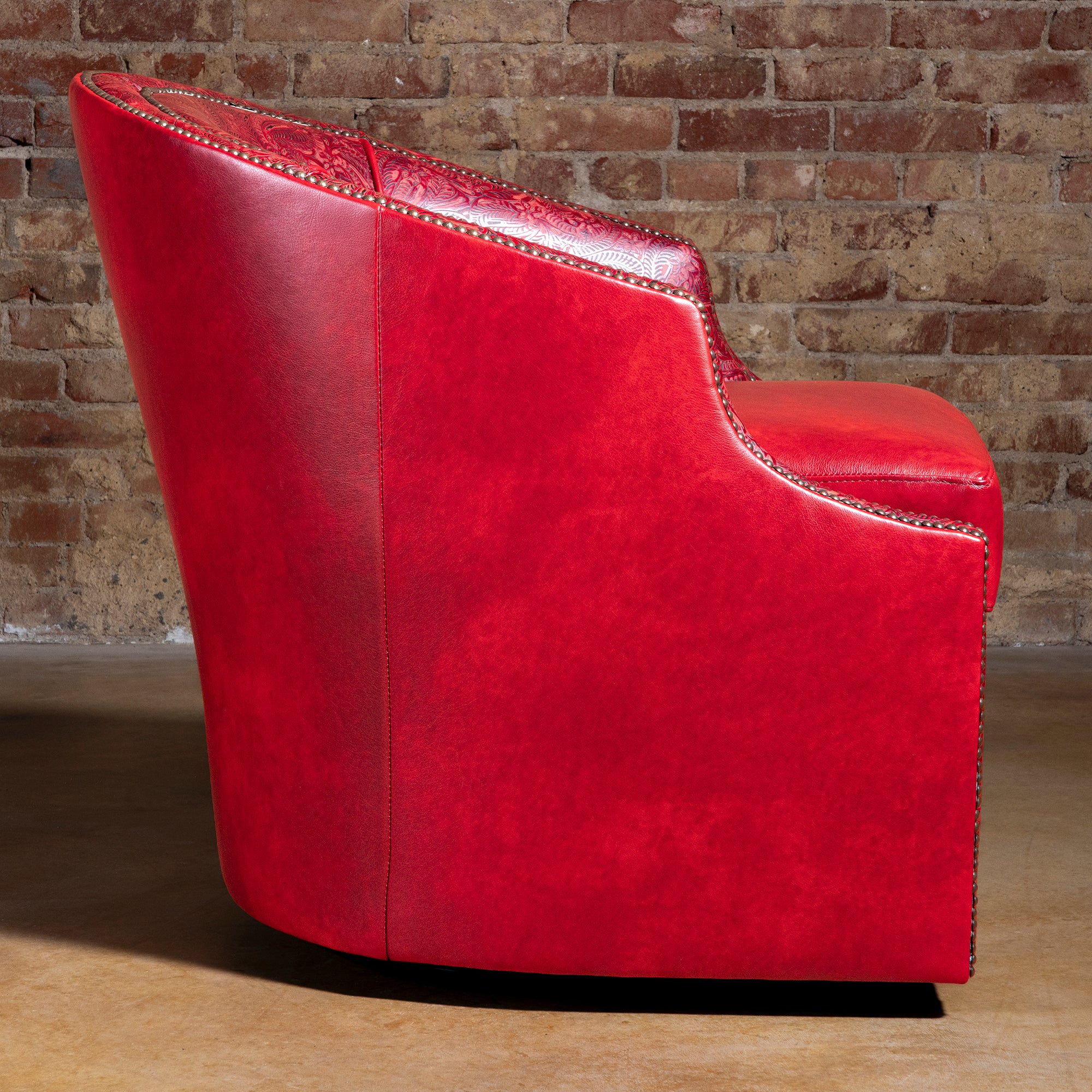Side profile of Vaquera Royale red leather barrel swivel chair against brick wall