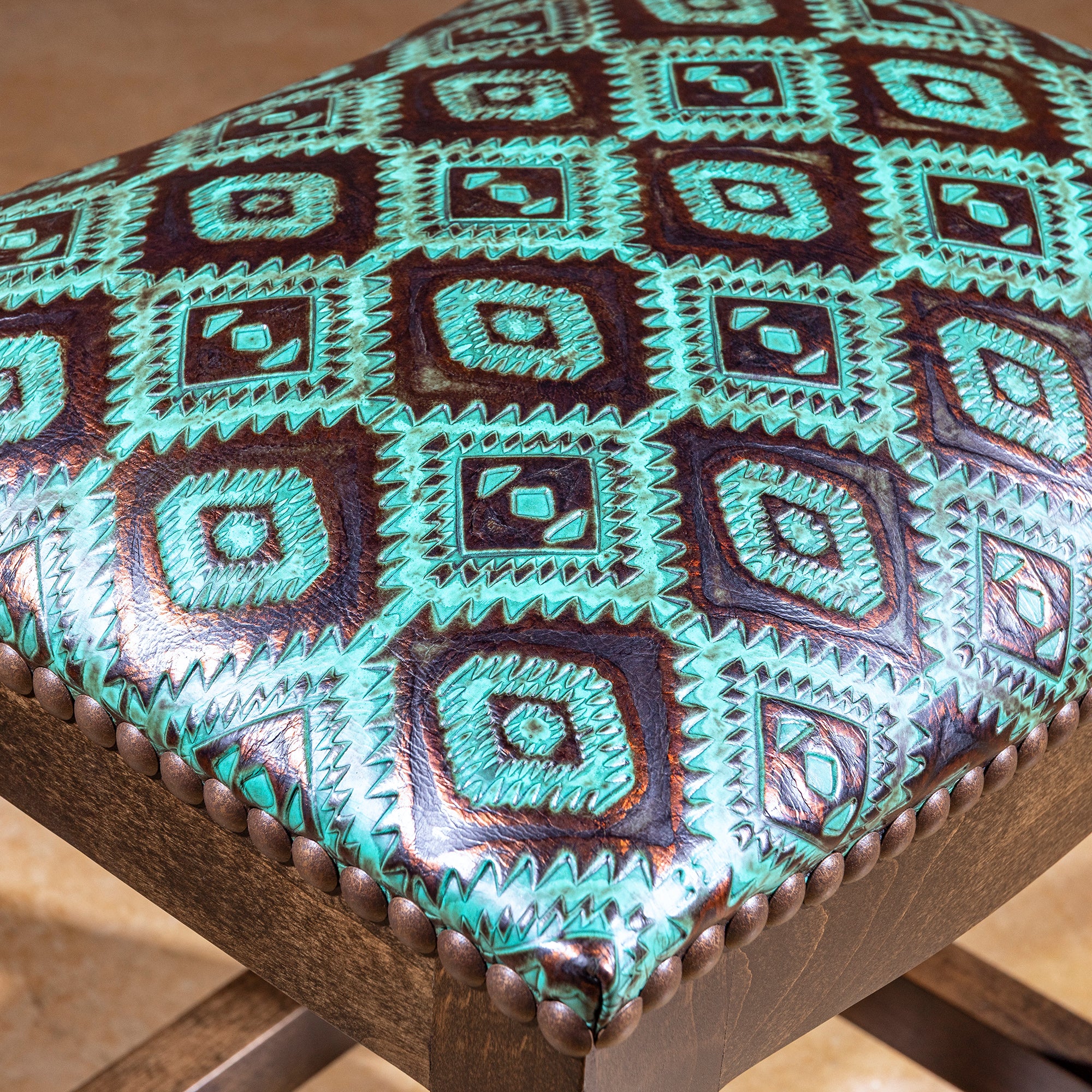 Verdigris Saddle Stool closeup of turquoise tooled leather, raised Western pattern, and bronze nailhead trim