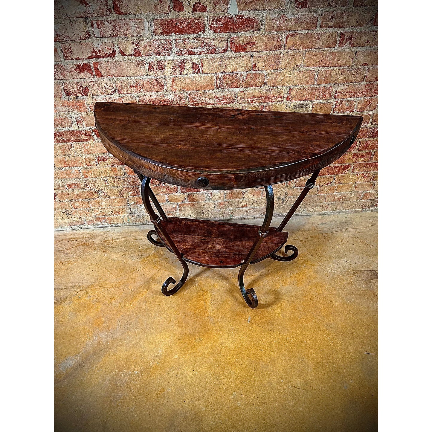 This Half Round Table is expertly crafted with a hand forged iron base, providing exceptional durability and a unique design. Its solid wood top adds a touch of natural beauty, while the wood shelf at the bottom offers additional storage space. A perfect choice for both style and function.