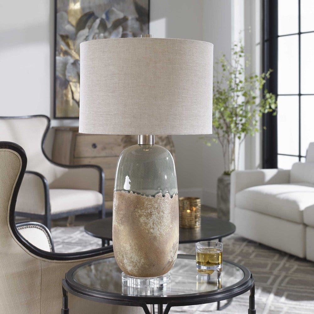 The Maggie Table Lamp's unique ceramic base features a terracotta rust finish with a crackled green-gray glaze, complemented by brushed nickel details and a thick crystal foot. The warm gray linen shade, with natural slubbing, provides a subtle yet stylish lighting effect to any room.