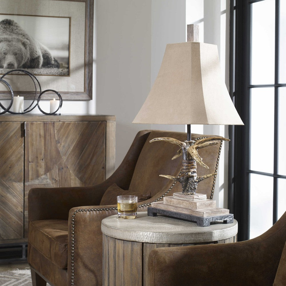 This Stag Horn Light Table Lamp is the perfect balance of modern and traditional aesthetics with its natural brown and ivory finish, scratched silver and cast aluminum accents, and a brushed palomino sueded shade with clipped corners. An ideal addition to any room.