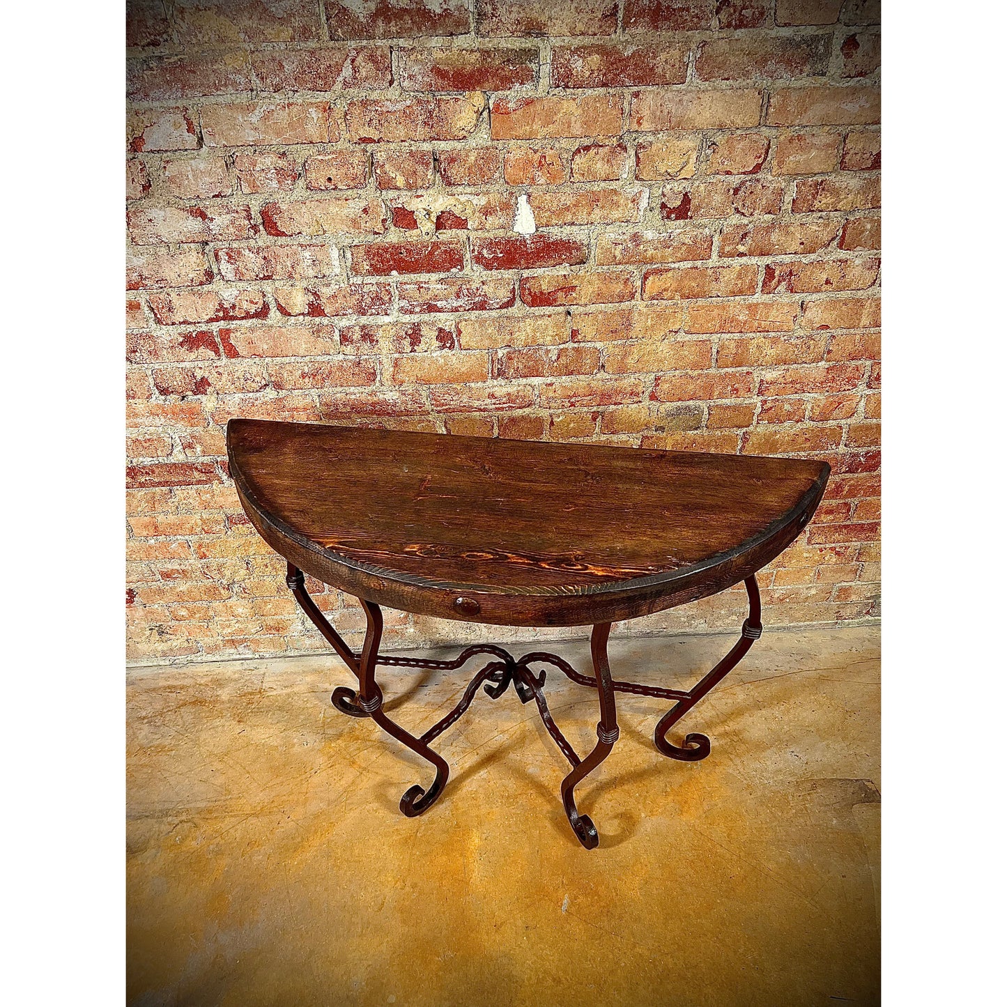 This hand forged iron half round table boasts a solid wood top and intricate swirled iron design. Perfect for adding a touch of elegance to any space. Expertly crafted with durable materials, this table is both functional and stylish.