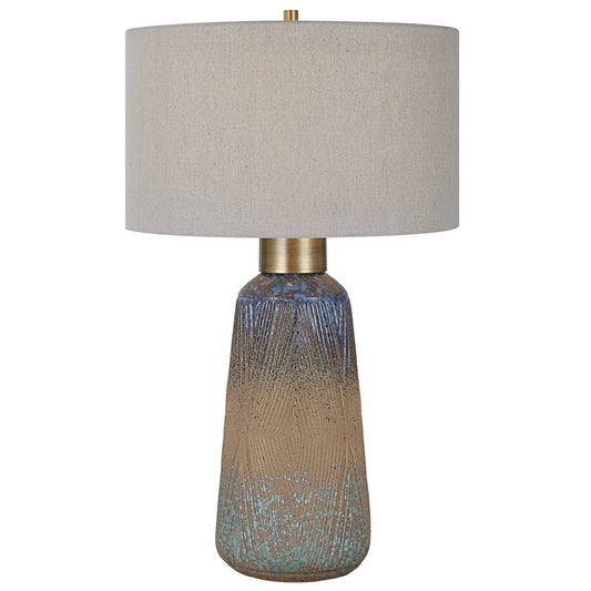 A beautiful display of color and style, this ceramic table lamp features an embossed design with a unique mix of matte and gloss glazes in various shades of blue-green, indigo, and golden rust, paired with antique brass plated details. The hardback drum shade is covered in a light gray linen fabric with natural slubbing.