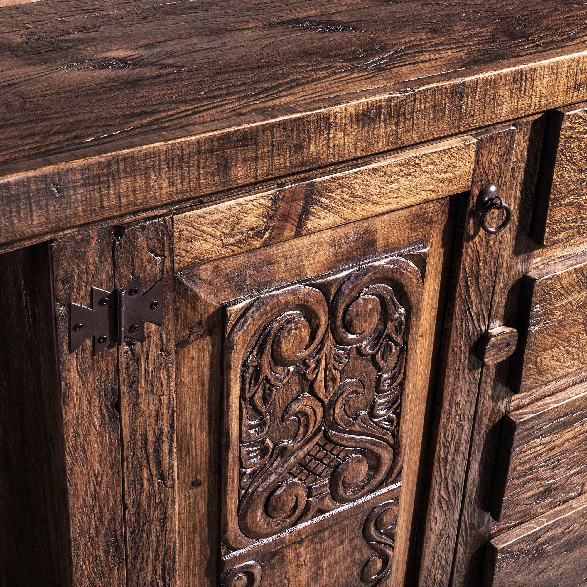 Close-up of hand-carved door panel and iron hinge on reclaimed wood buffet