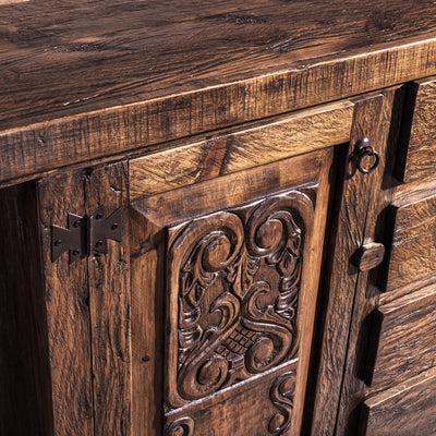 Close-up of hand-carved door panel and iron hinge on reclaimed wood buffet