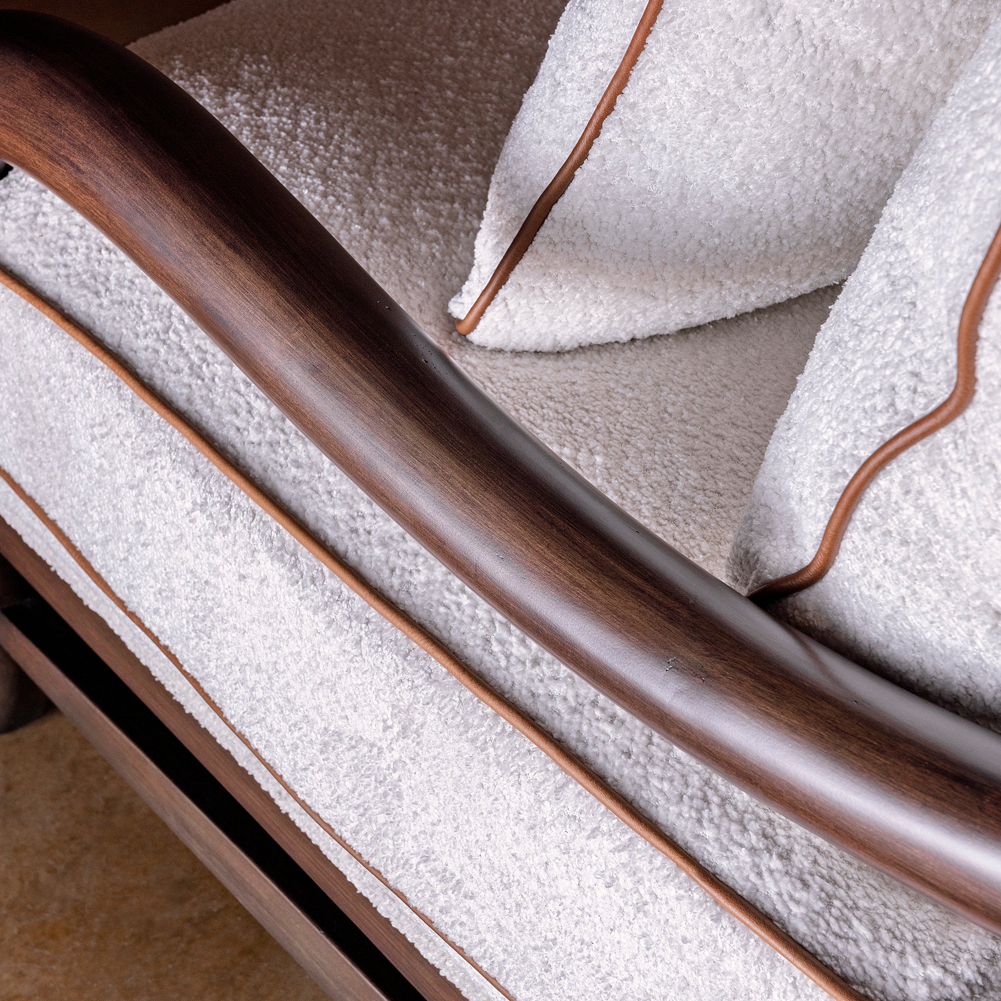 Closeup of stained wood arm on bouclé accent chair with leather piping detail