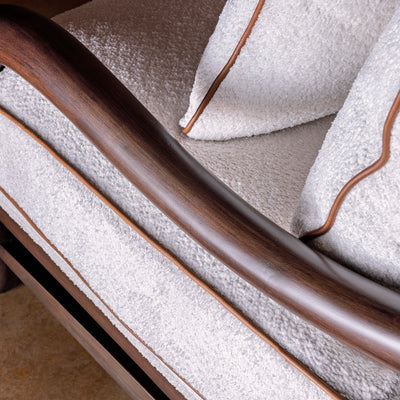 Closeup of stained wood arm on bouclé accent chair with leather piping detail