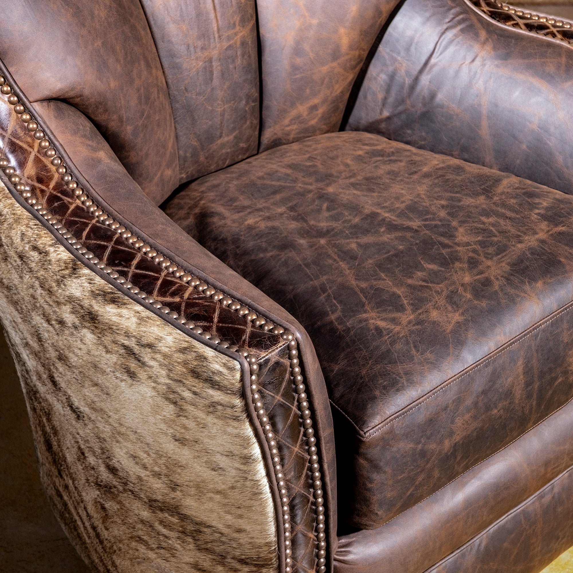 Brindle Cavalier Cowhide Western Swivel Chair close-up with distressed leather seat, cowhide panel, croc trim, and antique nailheads.