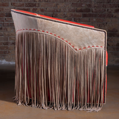 Profile view of coral-red leather barrel swivel chair with fringe and nailhead trim