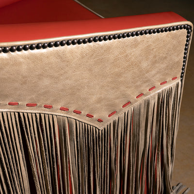 Closeup of taupe leather outside arm with coral red lacing and nailhead trim