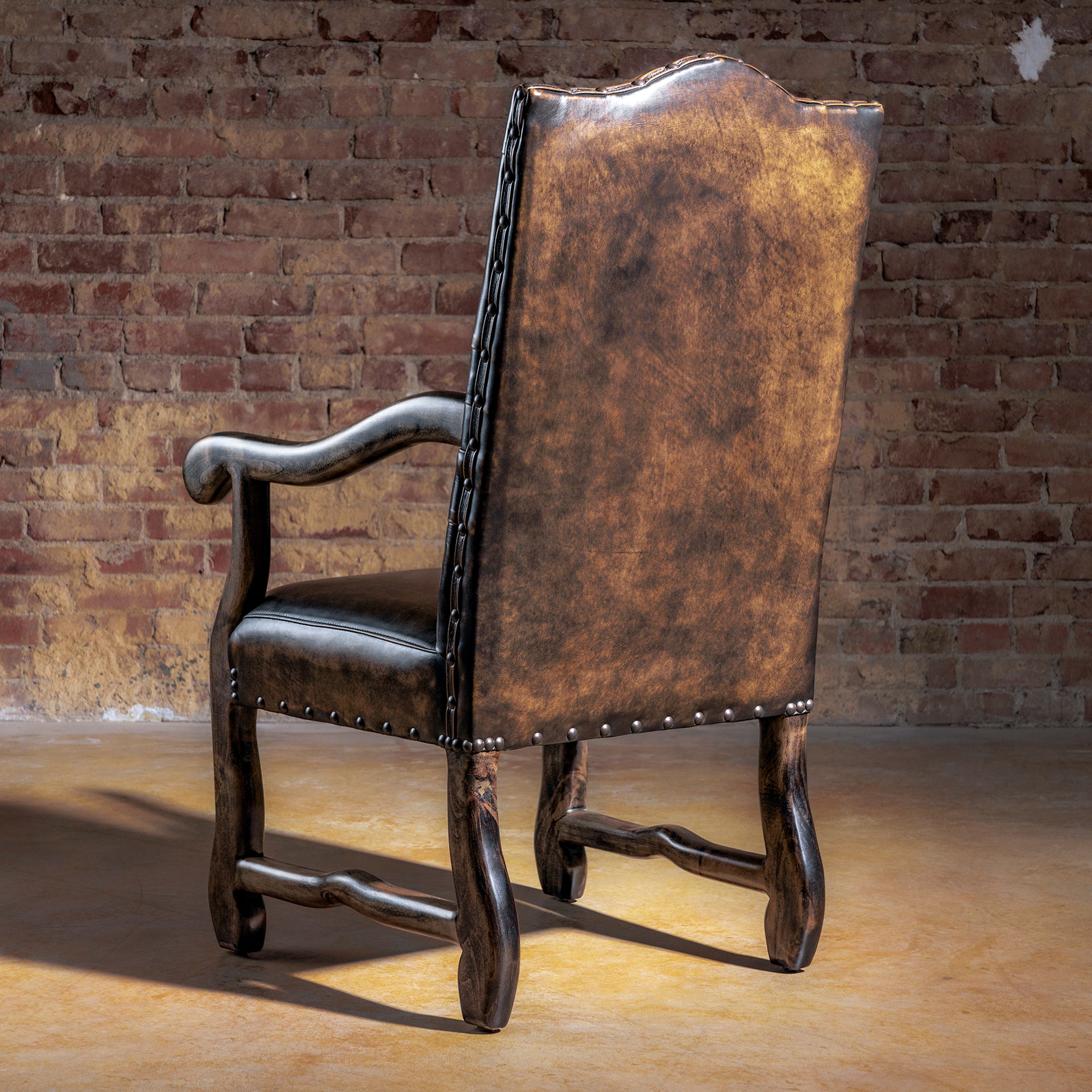 Back view of distressed brown leather Western arm chair with tall back, nailhead detailing, and solid wood legs.