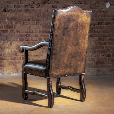 Back view of distressed brown leather Western arm chair with tall back, nailhead detailing, and solid wood legs.