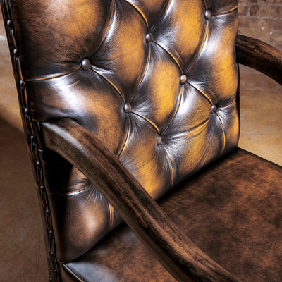 Button-tufted leather back detail on a Western arm chair with sculpted wood arm and rich brown patina finish.