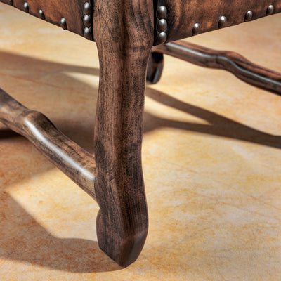 Ranch-finished wood leg and stretcher detail on a Western leather arm chair with nailhead accents and sturdy stance.