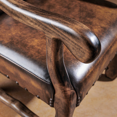 Sculpted ranch-finished wood arm detail on a brown leather Western arm chair—smooth curve with heirloom character.