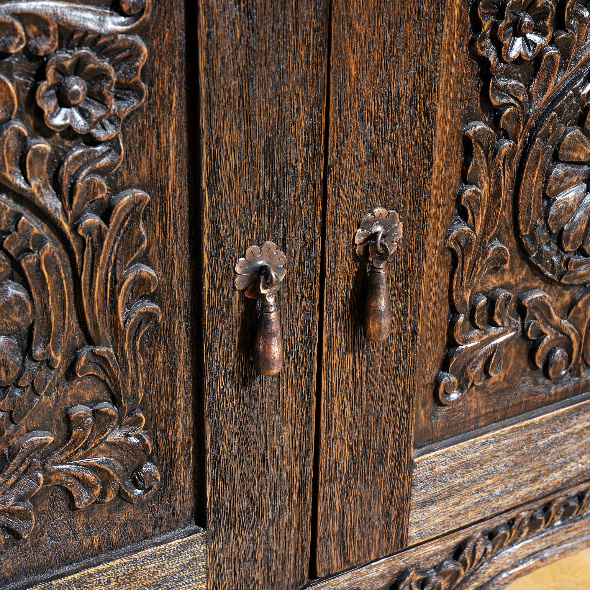 Carved wood cabinet doors with floral rosette relief and vintage-style iron pull handles on Western nightstand
