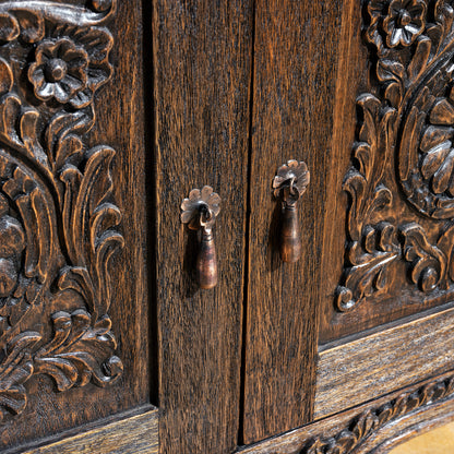 Carved wood cabinet doors with floral rosette relief and vintage-style iron pull handles on Western nightstand